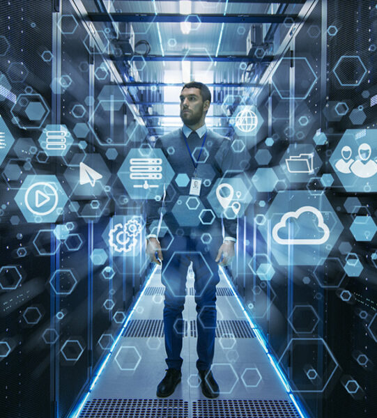 Curios IT Engineer Standing in the Middle of a Working Data Center Server Room. Cloud and Internet Icon Visualisation in the Foreground.